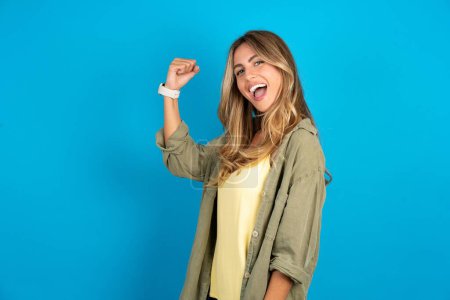 Photo for Profile side view portrait beautiful blonde woman wearing overshirt on blue background celebrates victory - Royalty Free Image