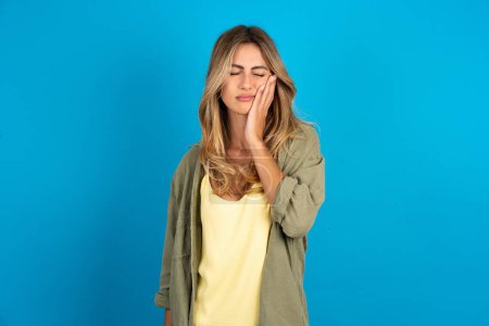 Photo for Young beautiful blonde woman wearing overshirt on blue background with toothache - Royalty Free Image