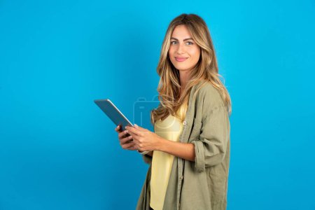 Photo for Photo of optimistic young beautiful blonde woman wearing overshirt on blue background hold tablet - Royalty Free Image