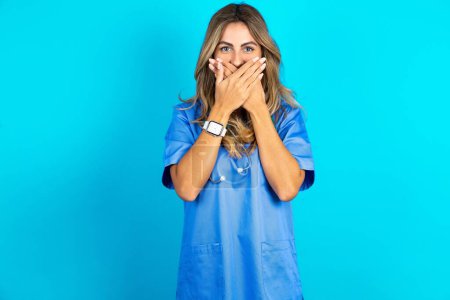 Photo for Beautiful doctor woman standing over blue studio background shocked covering mouth with hands for mistake. Secret concept. - Royalty Free Image