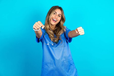 Photo for Beautiful doctor woman standing over blue studio background imagine steering wheel helm rudder passing driving exam good mood fast speed - Royalty Free Image