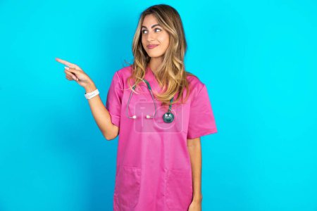 Téléchargez les photos : Femme caucasienne médecin en uniforme médical rose avec des points stéthoscope à l'espace de copie et annonce quelque chose, conseils meilleur prix. - en image libre de droit