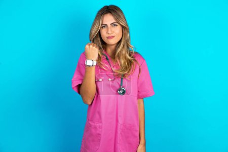 Téléchargez les photos : Femme caucasienne médecin en uniforme médical rose avec stéthoscope montre poing a ennuyé expression du visage va se venger ou menacer quelqu'un fait regard sérieux. Je vais vous montrer qui est le patron. - en image libre de droit
