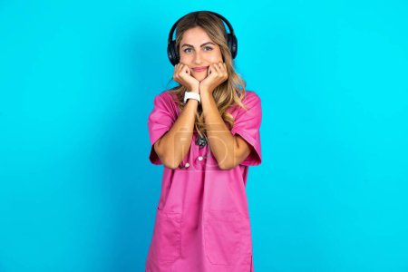 Photo for Portrait of sad  caucasian woman doctor in pink medical uniform with stethoscope in headphones - Royalty Free Image