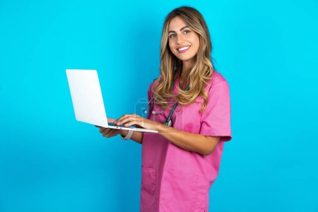 Téléchargez les photos : Adorable belle femme médecin debout sur fond bleu studio tenant dispositif moderne - en image libre de droit