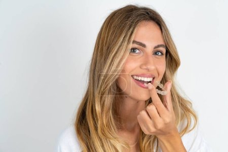 young caucasian businesswoman wearing white shirt over white background holding an invisible aligner ready to use it. Dental healthcare and confidence concept.