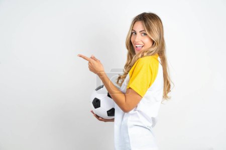 Téléchargez les photos : Photo de profil de jeune belle femme tenant ballon de football sur fond blanc indiquer doigt vide offre d'espace - en image libre de droit