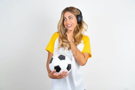 Foto de Positivo joven hermosa mujer sosteniendo pelota de fútbol sobre fondo blanco anuncio promo toque dientes de dedo - Imagen libre de derechos