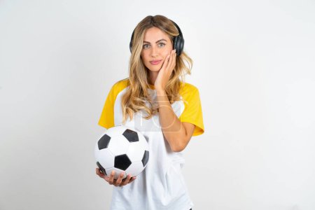 Téléchargez les photos : Photo de jeune belle femme tenant ballon de football sur fond blanc profiter fraîche parfaite peau lisse toucher visage - en image libre de droit