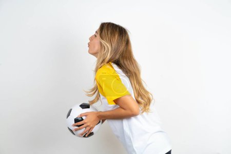Téléchargez les photos : Profil vue de côté, portrait d'attrayant jeune belle femme tenant ballon de football sur fond blanc envoyant baiser d'air - en image libre de droit