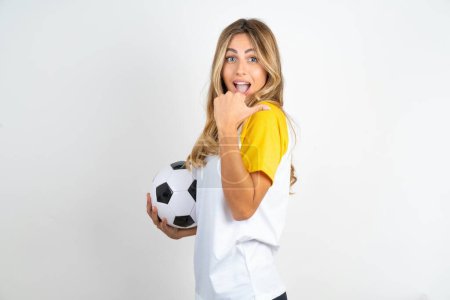 Foto de Impresionante hermosa mujer con camiseta de fútbol sobre fondo blanco punto atrás espacio vacío sosteniendo pelota de fútbol - Imagen libre de derechos