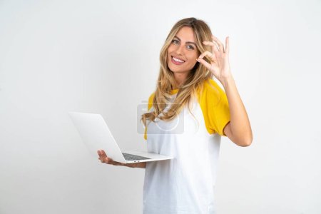 Foto de Positiva hermosa mujer con camiseta de fútbol sobre fondos blancos netbook inalámbrico muestra símbolo okey - Imagen libre de derechos