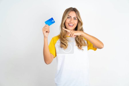Foto de Sonriente caucásica hermosa mujer usando fútbol camiseta sobre fondo blanco mostrando tarjeta de débito - Imagen libre de derechos