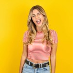 Beautiful blonde young woman wearing striped t-shirt over yellow studio background winking looking at the camera with sexy expression, cheerful and happy face. 