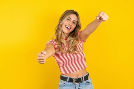 Photo for Beautiful blonde young woman wearing striped t-shirt over yellow studio background imagine steering wheel helm rudder passing driving exam good mood fast speed - Royalty Free Image