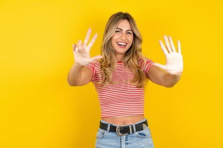Photo for Young beautiful blonde woman wearing striped t-shirt over yellow studio background showing and pointing up with fingers number eight while smiling confident and happy. - Royalty Free Image
