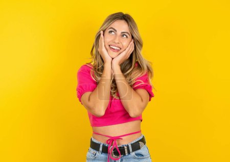 Photo for Inspired blonde young woman wearing pink crop top on yellow background looking at copyspace having thoughts about future events - Royalty Free Image
