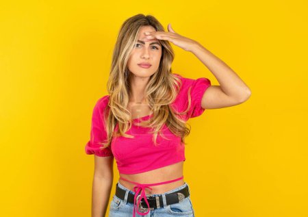 Photo for Beautiful blonde young woman wearing pink crop top on yellow background pointing unhappy at pimple on forehead, blackhead  infection. Skincare concept. - Royalty Free Image