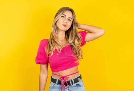 Photo for Beautiful blonde young woman wearing pink crop top on yellow background being confused and wonders about something. Holding hand on head, uncertain with doubt. Pensive concept. - Royalty Free Image