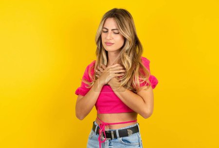 Photo for Sad blonde young woman wearing pink crop top on yellow background desperate and depressed with tears on her eyes suffering pain and depression in sadness facial expression and emotion concept - Royalty Free Image