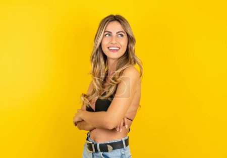 Photo for Beautiful young blonde woman wearing bikini over yellow background crosses arms looks at empty space - Royalty Free Image