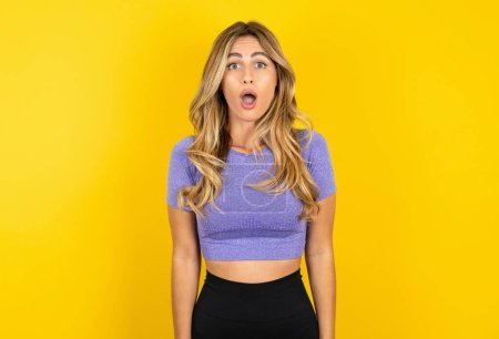 Photo for Shocked young woman wearing sportswear over yellow studio background has surprised expression. Omg concept - Royalty Free Image