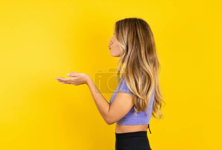 Téléchargez les photos : Portrait de profil de jeune femme attrayante portant des vêtements de sport sur fond jaune studio envoyer baiser air - en image libre de droit