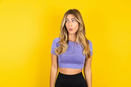 Photo for Stunned young woman wearing sportswear over yellow studio background stares reacts on unexpected news - Royalty Free Image