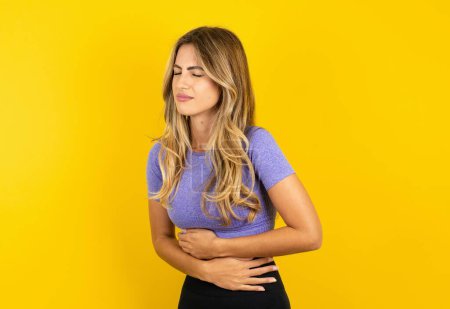 Téléchargez les photos : Jeune femme portant des vêtements de sport sur fond jaune studio souffrant de maux d'estomac - en image libre de droit