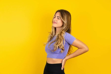 Téléchargez les photos : Jeune femme blonde portant des vêtements de sport sur fond jaune studio souffrant de maux de dos - en image libre de droit