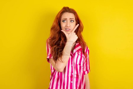 Photo for Red haired woman wearing pink pyjama over yellow studio background thinking worried about a question, concerned and nervous with hand on chin. - Royalty Free Image