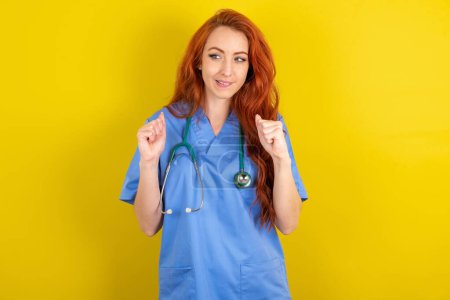 Photo for Young red-haired doctor woman clenches fists and awaits for something nice happened looks away bites lips and waits announcement of results - Royalty Free Image