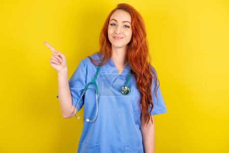 Photo for Positive young red-haired doctor woman with satisfied expression indicates at upper right corner shows good offer suggests to click on link - Royalty Free Image