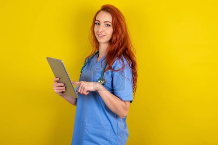 Téléchargez les photos : Photo de heureuse jeune femme rousse médecin tenir tablette navigation sur Internet - en image libre de droit