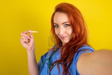Téléchargez les photos : Jeune femme médecin aux cheveux roux faire selfie tenant un aligneur de bretelles invisible, recommandant ce nouveau traitement. Concept de soins dentaires. - en image libre de droit