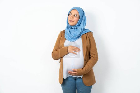 Foto de Musulmana embarazada mujer usando hijab mirando a un lado en el espacio vacío pensativo - Imagen libre de derechos
