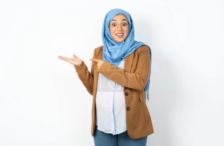 Téléchargez les photos : Musulmane enceinte femme portant hijab pointant et tenant la main montrant annonces - en image libre de droit