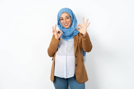 Téléchargez les photos : Femme enceinte musulmane portant hijab montrant les deux mains avec les doigts en signe OK. Approbation ou recommandation du concept - en image libre de droit