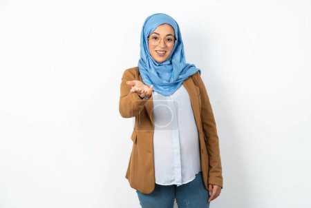 Téléchargez les photos : Musulmane enceinte femme portant hijab souriant joyeuse offrant main de paume donnant assistance et acceptation. - en image libre de droit