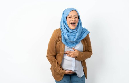 Photo for Muslim pregnant woman wearing hijab smiling and laughing hard out loud because funny crazy joke with hands on body. - Royalty Free Image