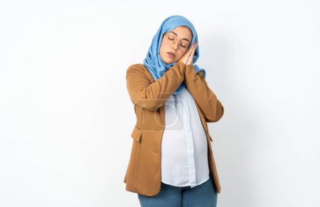 Téléchargez les photos : Musulmane enceinte femme portant hijab dormir fatigué rêver et posant avec les mains ensemble tout en souriant avec les yeux fermés. - en image libre de droit