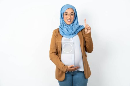 Photo for Muslim pregnant woman wearing hijab showing and pointing up with finger number one while smiling confident and happy. - Royalty Free Image