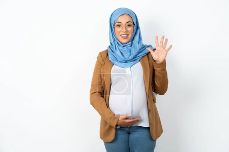 Téléchargez les photos : Musulmane enceinte femme portant hijab montrant et pointant vers le haut avec les doigts numéro cinq tout en souriant confiant et heureux. - en image libre de droit