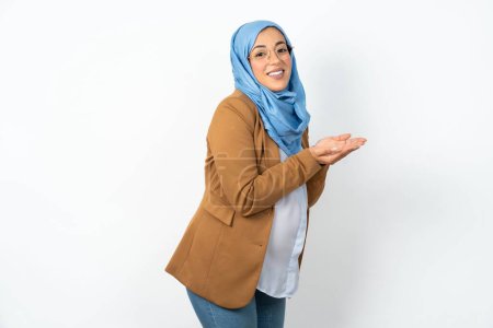 Téléchargez les photos : Musulmane enceinte femme portant hijab pointant vers le côté avec les mains ouvertes paumes montrant l'espace de copie, présentant la publicité souriant heureux excité - en image libre de droit