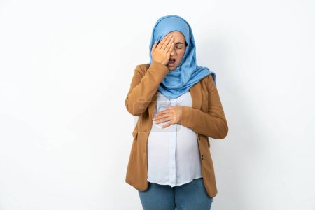 Foto de Mujer musulmana embarazada con hiyab bostezando cansada cubriendo media cara, ojos y boca con la mano. La cara duele de dolor. - Imagen libre de derechos