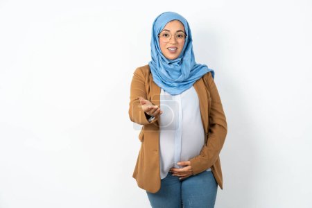 Foto de Musulmana embarazada vistiendo hijab sonriente amistoso ofreciendo apretón de manos como saludo y bienvenida. Negocios exitosos. - Imagen libre de derechos