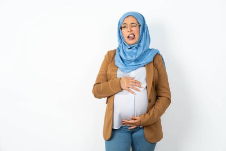 Téléchargez les photos : Musulmane enceinte femme portant hijab langue collante heureux avec expression drôle. Concept d'émotion. - en image libre de droit