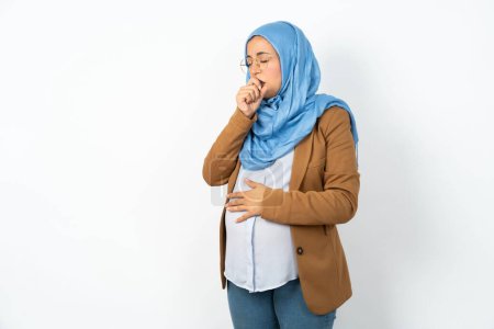Téléchargez les photos : Femme musulmane enceinte portant le hijab se sentant mal et toussant comme symptôme du rhume ou de la bronchite. Concept de soins de santé. - en image libre de droit