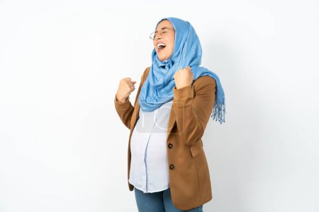 Téléchargez les photos : Femme musulmane enceinte portant hijab célébrant surpris et étonnés pour le succès avec les bras levés et les yeux fermés. Concept gagnant. - en image libre de droit