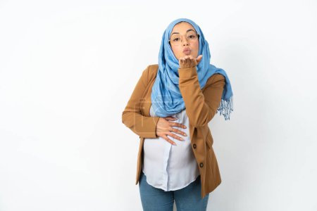 Photo for Beautiful pregnant muslim woman wearing hijab looking at the camera blowing a kiss with hand on air being lovely . Love expression. - Royalty Free Image